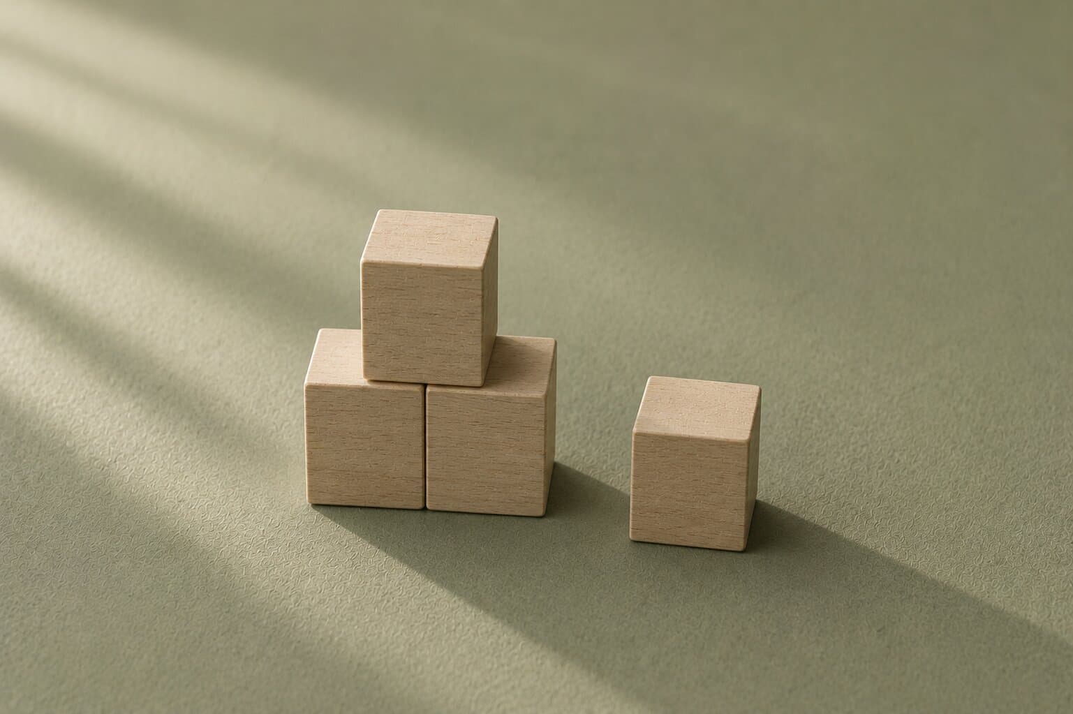 Pale wooden building blocks part-assembled with one block set apart on a soft sage-green surface