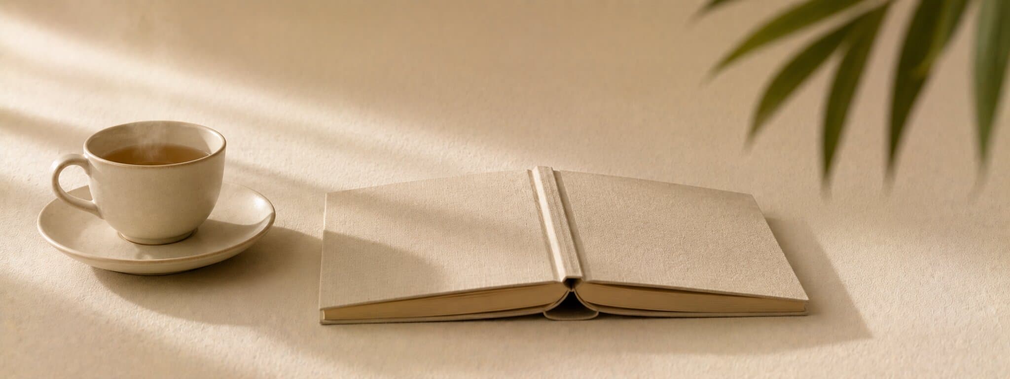 Editorial still life of a teacup, open book and a soft plant leaf